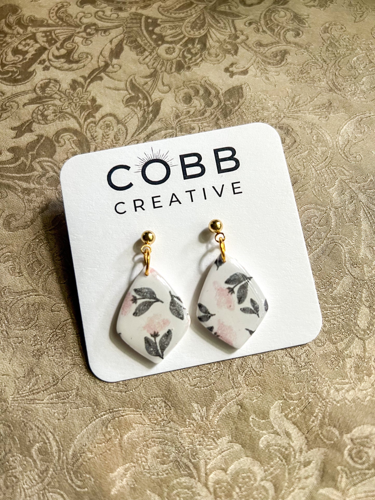 Floral patterned earrings on a branded card against a textured background