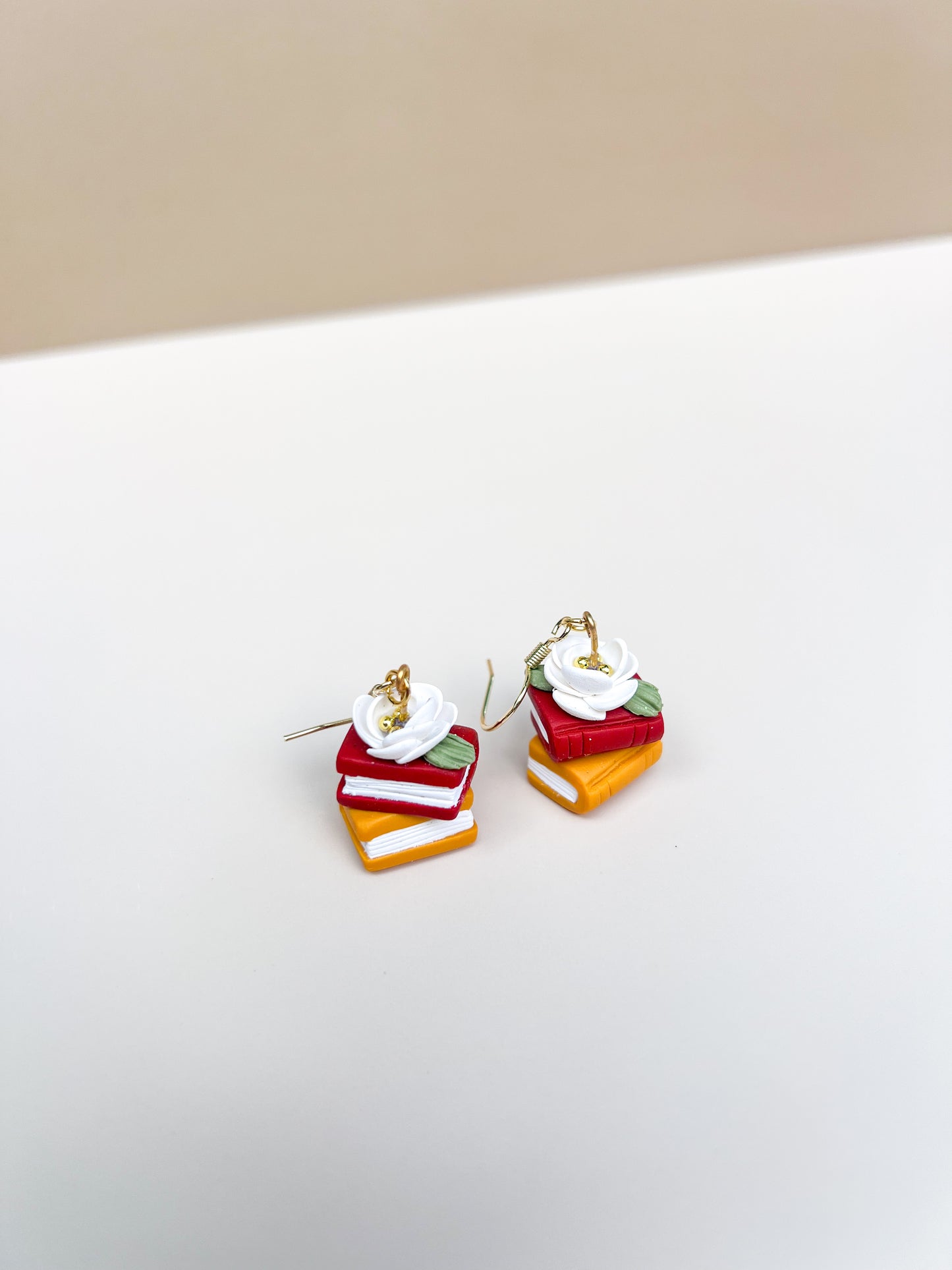 Stacked colorful book earrings on a white surface with a beige background