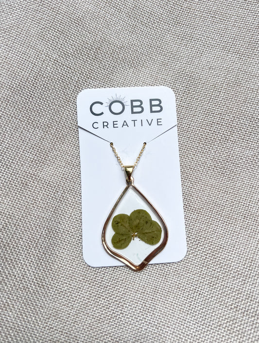 Necklace with a four-leaf clover pendant on a COBB CREATIVE card against a textured gray background