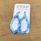Blue and white marbled earrings on a COBB CREATIVE card against a wooden background