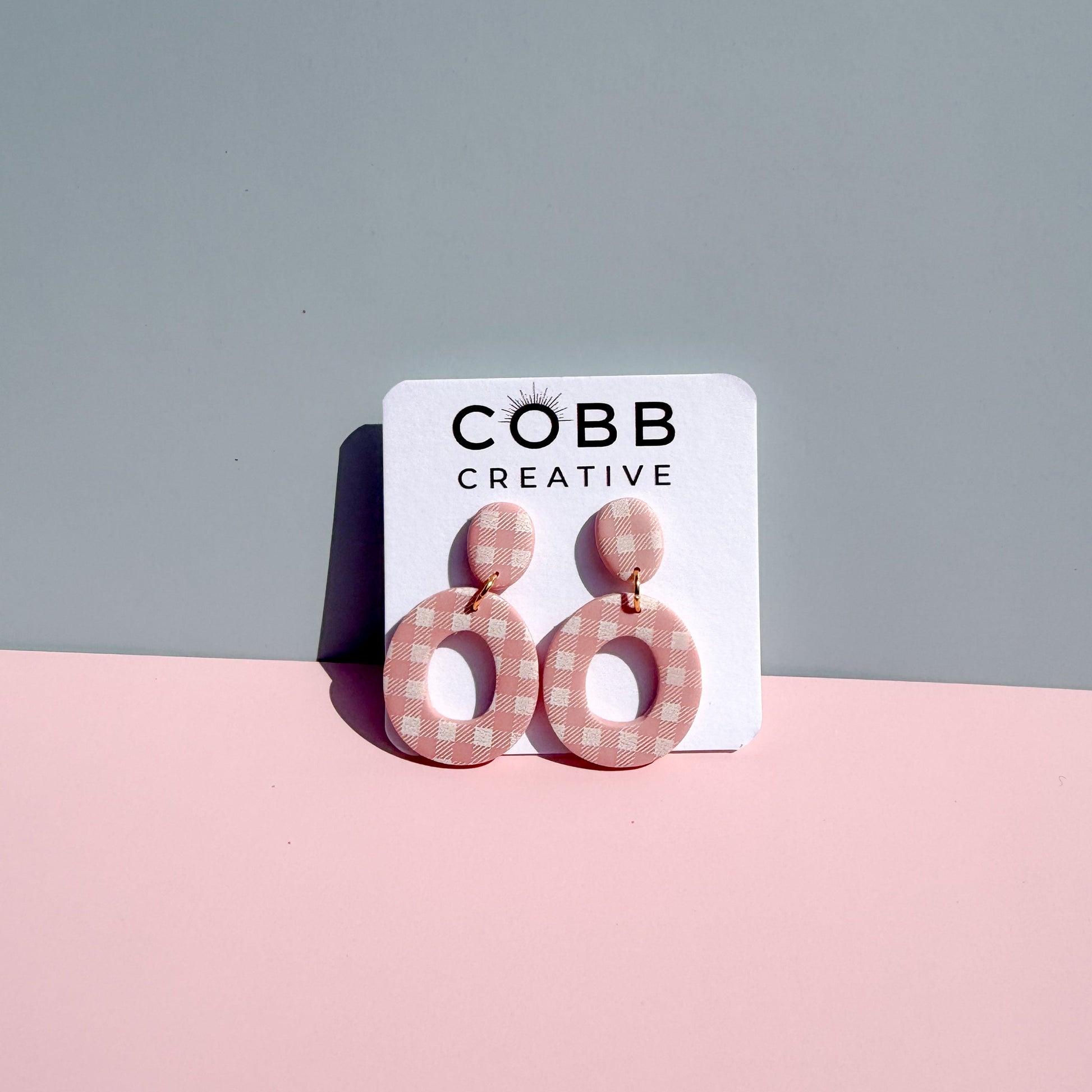 Pair of pink gingham earrings on a COBB Creative branded card against a gray background