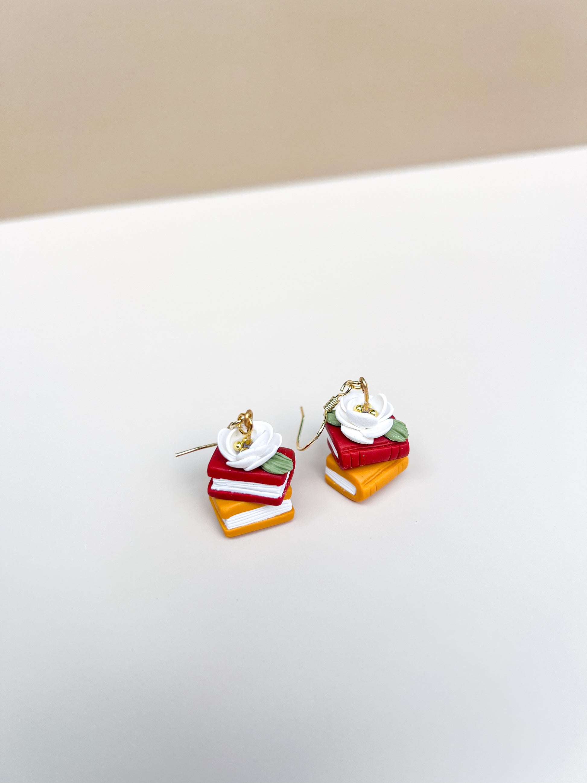 Stacked colorful book earrings on a white surface with a beige background