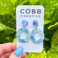 Blue marbled earrings on a Cobb Creative card held against a green leafy background