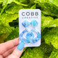 Blue marbled earrings on a Cobb Creative card held against a green leafy background