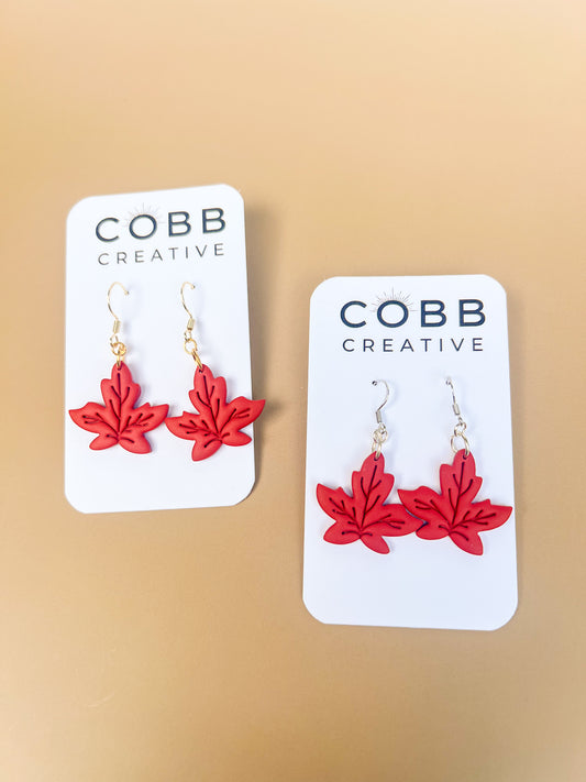 Red leaf-shaped earrings on Cobb Creative branded cards against a beige background.