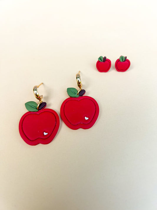 Red apple-shaped earrings with green leaves on a beige background